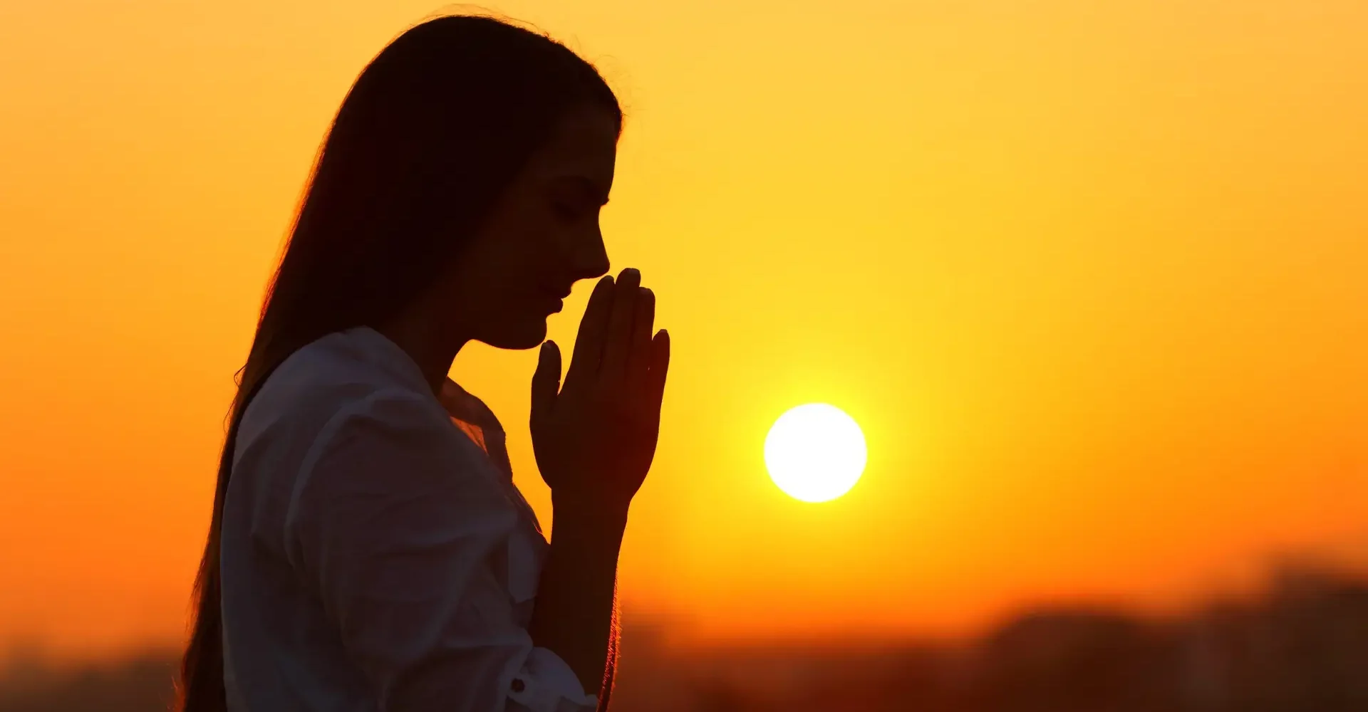 Side view backlight portrait of a woman silhouette praying at sunset