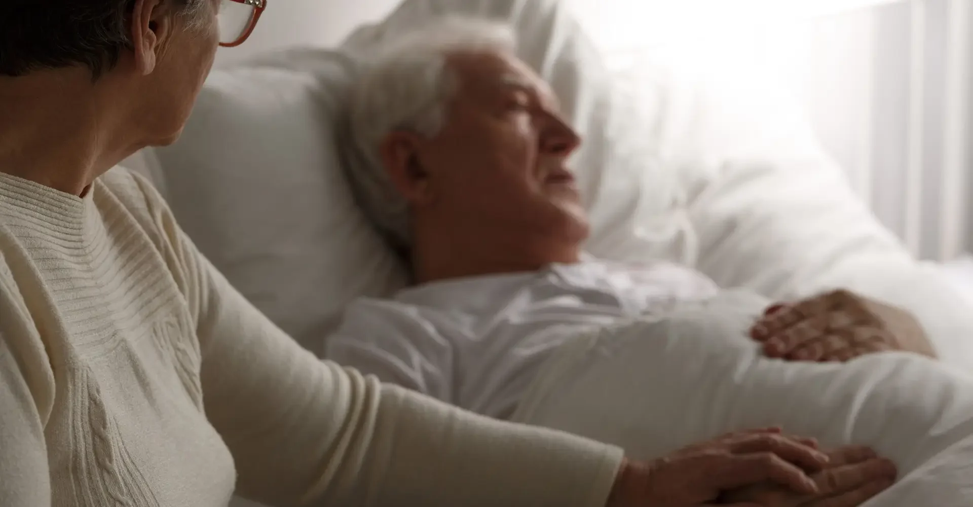 Sad senior man in hospital bed and his wife sitting next to him